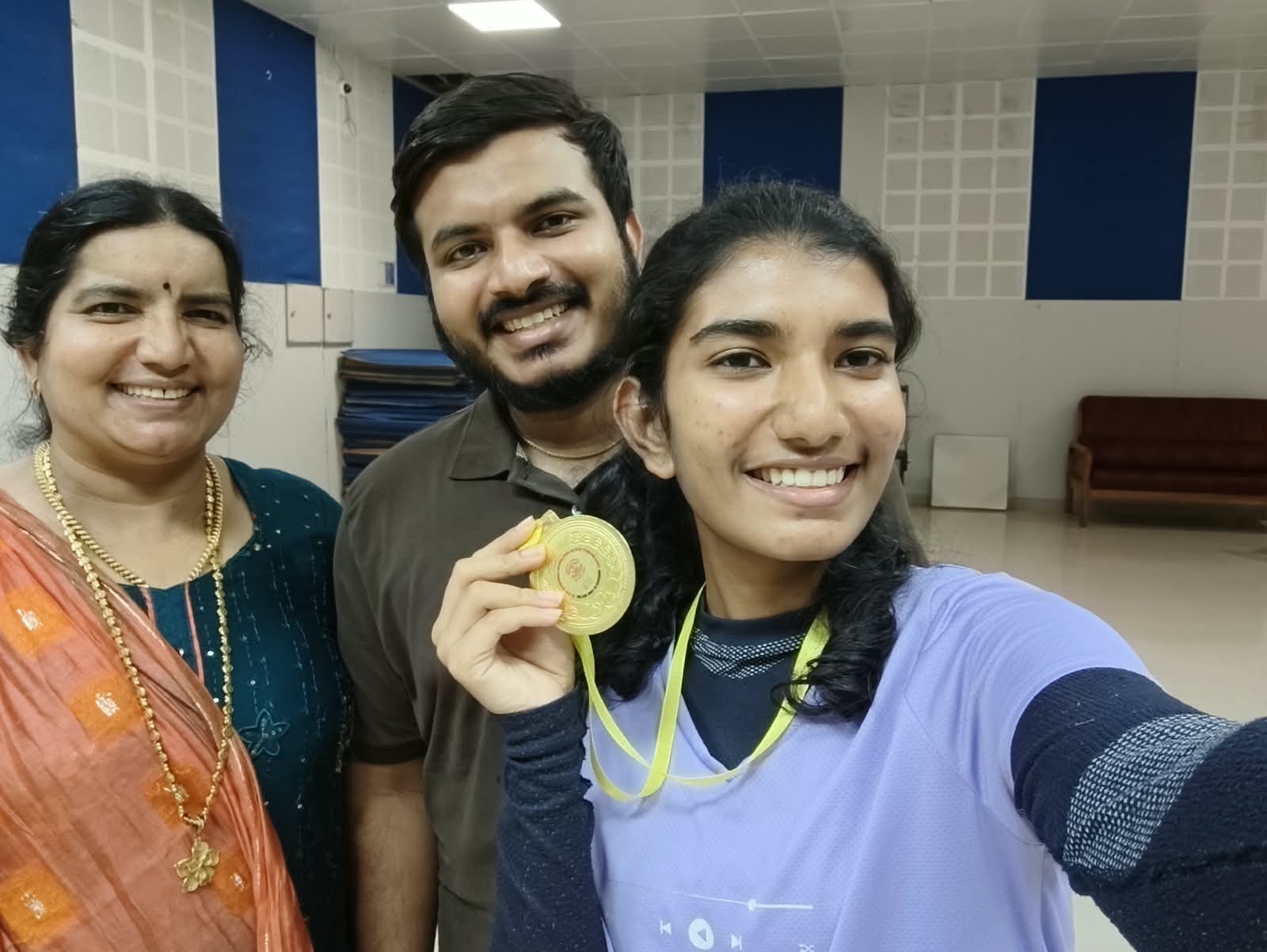 Brahmitha G taking a selfie with two family members, holding up her gold medal