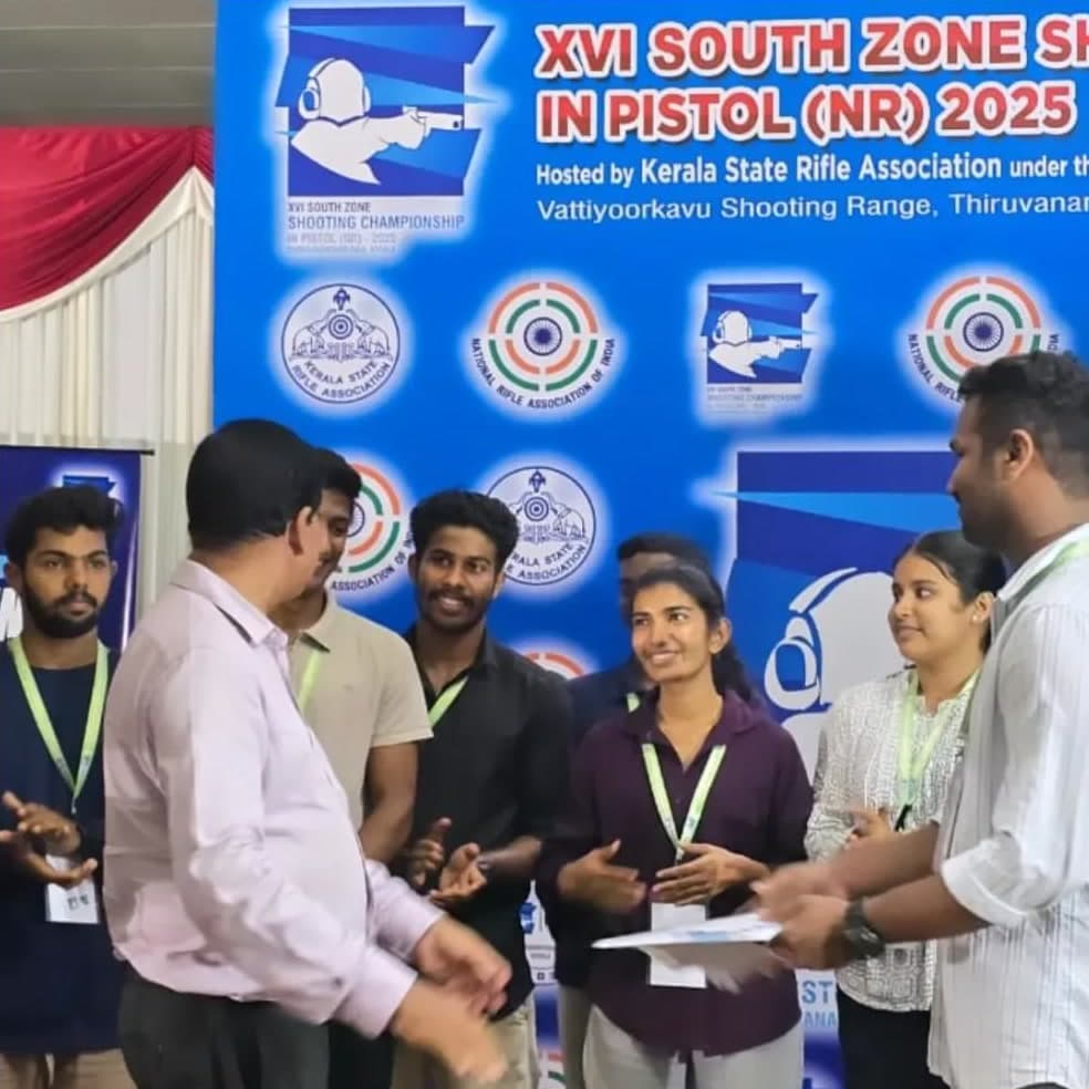 Brahmitha G among a group in front of the XVI South Zone Shooting Championship in Pistol banner